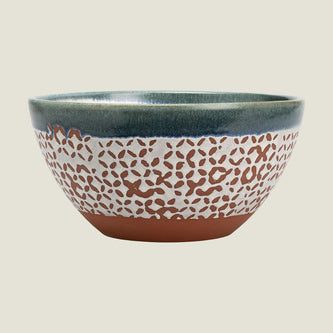 A handmade ceramic bowl with a speckled terracotta pattern on a cream body, featuring a dark teal glazed rim and base.