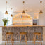 Modern kitchen with stone countertop, wooden stools, and pendant lights.