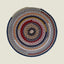 Round braided rug with concentric circles of multicolored yarn on a beige background