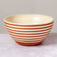 A round ceramic bowl with horizontal terracotta orange stripes on an off-white glazed exterior, shown on a light gray surface against a neutral gray background.