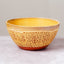 A handmade ceramic bowl with a textured, speckled yellow exterior and a smooth, glossy yellow interior, set against a neutral gray background.