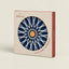 A square product box for a C'Atlántica hot pot stand/salvamanéles, featuring a circular cutout that displays the navy blue and white starburst design of the product. The box is made of a textured beige paperboard with coral-red side panels and printed branding.