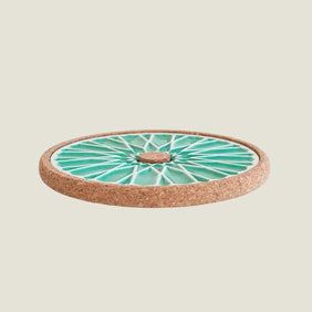 Round trivet with green ceramic top and cork base on a white background