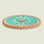 A round ceramic trivet or coaster with a turquoise and white geometric wheel design and a natural cork border, shown on a light beige background.