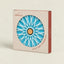 C Atlántica brand hot pot stand in its original packaging, featuring a circular cutout that reveals a blue and white starburst design with a cork center, set against a solid light beige background.
