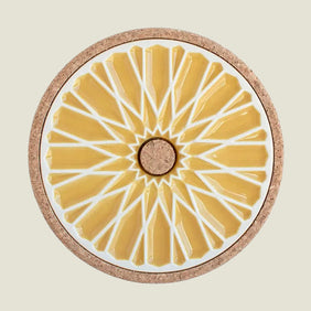 Round coaster with yellow sunburst design and cork back on a beige background