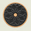 A round cork coaster with a black textured center featuring an embossed floral mandala pattern and a small cork circle in the middle, shown on a light beige background.