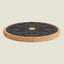 A round cork coaster with a black textured center featuring a floral pattern, shown on a solid light beige background.