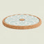 A round cork trivet or coaster with a light blue and white floral pattern on top, shown on a solid pale green background.