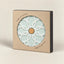 A square kraft paper gift box with a circular cutout window displaying a pale mint-green ceramic pot base with a white geometric floral pattern and a small cork center. The box has black side panels and printed text reading 'KERAMIC POT BASE' and 'MADE IN PORTUGAL'.