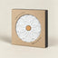 A square kraft paper box with a circular cutout showing a white ceramic pot base with an embossed floral pattern and a small cork center. The box has black side panels and printed text reading 'TERAMIC HOT POT BASE' and 'MADE IN PORTUGAL'.