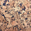 A close-up texture of cork material with a natural tan, brown, and beige grain pattern interspersed with dark blackish inclusions.