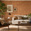 A styled living room interior featuring a white sofa with brown and olive green pillows, a dark wood coffee table, a mid-century armchair, and a textured cork wall backdrop.