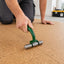 A person kneels on a cork floor while using a green and silver floor roller tool to flatten the cork tiles.
