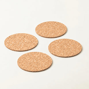Four round cork coasters in natural tan color arranged in a loose square on a clean white background.