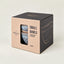A set of two small ceramic bowls by Atlantica, presented in a minimalist kraft paper and black cardboard gift box. The bowls feature a speckled blue and white glaze with a brown rim, visible through a clear window on the front of the packaging.