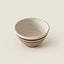 A small handmade ceramic bowl with a speckled off-white interior and exterior decorated with horizontal dark red stripes near the base, set against a solid light beige background.