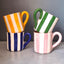 Four colorful striped mugs stacked against a gray background