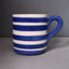 A ceramic mug with a blue and white striped pattern, featuring a thick handle and a textured glaze, set against a dark gray background.