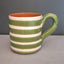 A ceramic mug with horizontal green and white stripes, featuring a glossy green handle and a terracotta-colored interior, set against a dark gray background.