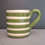 A ceramic mug with horizontal green and white stripes, featuring a thick green handle, set against a dark gray background.