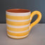 A ceramic mug with horizontal yellow and white stripes, featuring a solid yellow handle and a terracotta-colored interior, set against a dark gray background.
