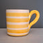 A ceramic mug with horizontal yellow and white stripes, featuring a thick, curved yellow handle, set against a dark gray background.