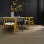 Dining table with yellow chairs and a vase of yellow flowers against a dark wall.