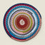 A round handwoven braided rug with concentric rings of multicolor yarn, including navy, teal, pink, gray, olive green, rust orange, and cream, shown on a light beige background.