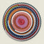 A round, hand-crocheted rug with concentric rings of multiple colors including pink, purple, red, orange, blue, green, and white, shown flat against a light beige background.