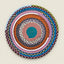 A round braided rope mat with concentric rings of multiple colors, including teal, pink, orange, gray, purple, blue, green, and white, photographed flat against a light beige background.
