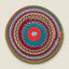 A round, handwoven braided placemat with concentric circular patterns in multiple colors including teal, red, pink, blue, green, and orange, shown on a solid light beige background.