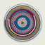 A round handwoven braided placemat with concentric rings of blue, pink, red, gray, green, orange, and white yarn, centered on a light beige background.