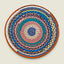 A round, handwoven braided rug with concentric rings of orange, brown, white, blue, teal, pink, and gray yarn, photographed flat against a solid light beige background.
