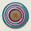 A round braided rope placemat with concentric circles of multicolor yarn, photographed flat against a light beige background.